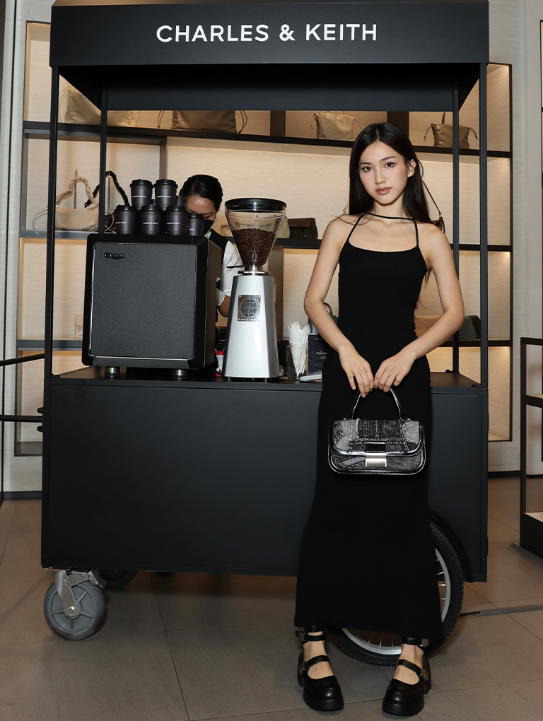 Soopanha poses in front of the coffee pushcart wearing the Charlot patchwork denim elongated top handle bag in noir and Robbie Denim-Effect Ankle-Strap Mary Jane boots — CHARLES & KEITH