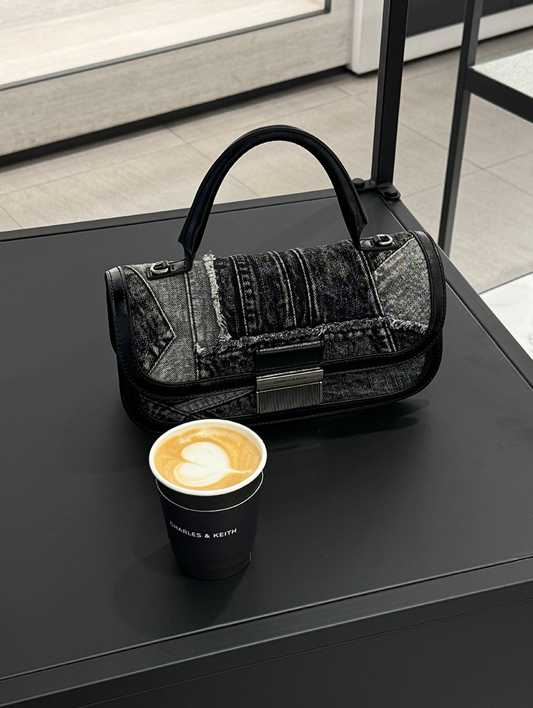 A cup of coffee with the Charlot patchwork denim elongated top handle bag in noir — CHARLES & KEITH