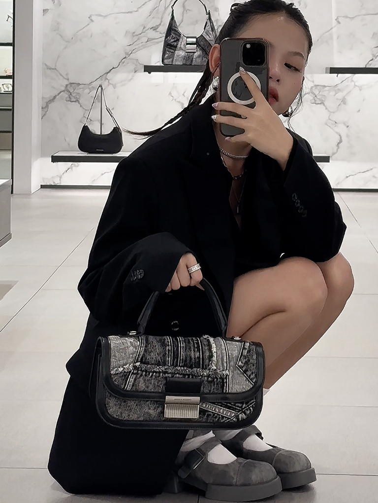 V Spring takes a photo of her wearing the Charlot patchwork denim elongated top handle bag in noir and Robbie Denim-Effect Ankle-Strap Mary Jane boots in dark grey — CHARLES & KEITH